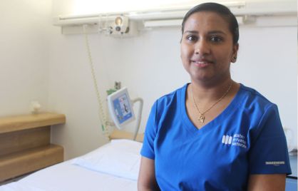 Beena Sasi is standing in front of a hospital bed and other medical equipment. She is smiling and wearing a blue Mater Private Network uniform.