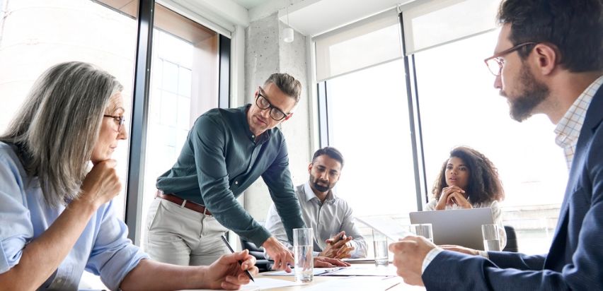 A group of men and women are discussing work related issues around a table in a bright office.