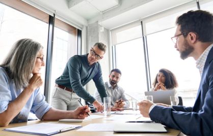 A group of men and women are having a work related discussion around a table in a bright office.