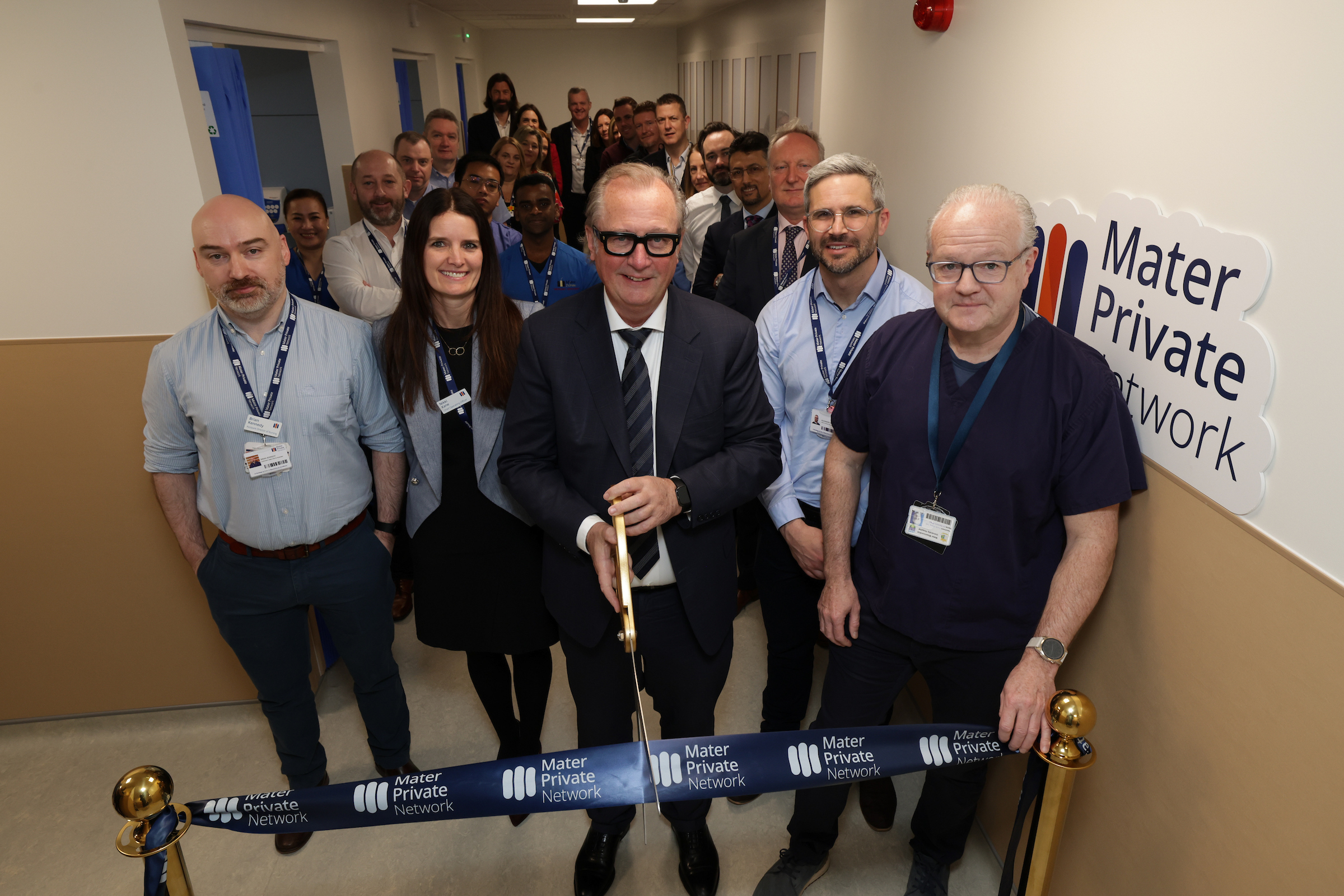 Mater Private Network CEO John Hurley officially opens new Emergency Department Bays at Eccles Street in Dublin. He is cutting a navy Mater Private ribbon with large scissors and is surrounded by staff.