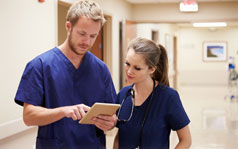 working-with-mpn-238x149 A female and male medical professionals in a hospital looking at a tablet together.