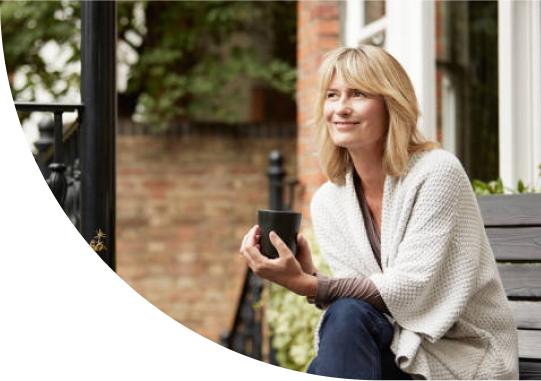 A woman is sitting outside a building on a bench holding a mug in her hands.