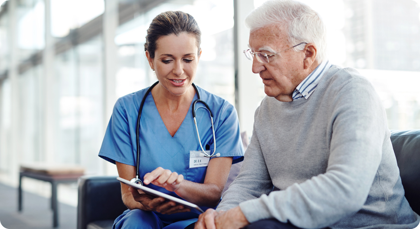 Urgent care image A female medical professional is sitting beside an older man. She is pointing to and showing the man something on a tablet.