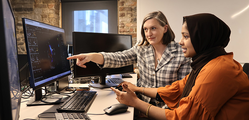 Amy sitting with a member of her team and she's pointing to a heart scan on a computer screen