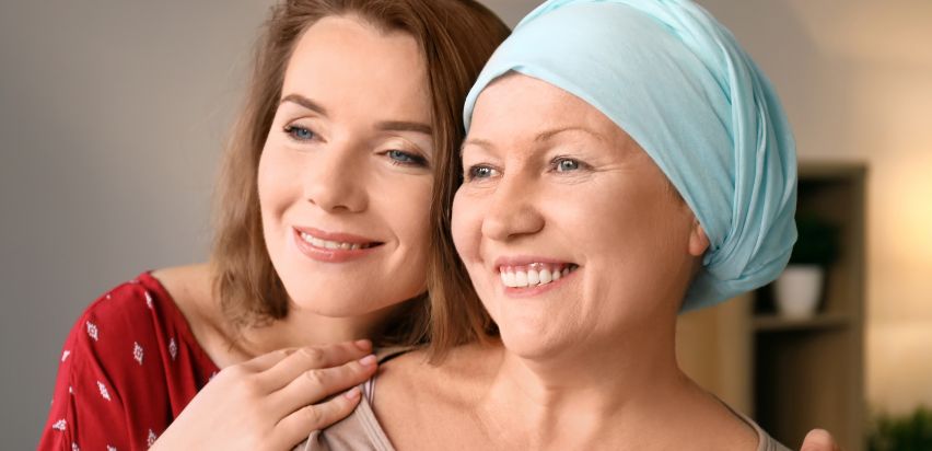 Two women, one of which is a cancer patient, are hugging and smiling.