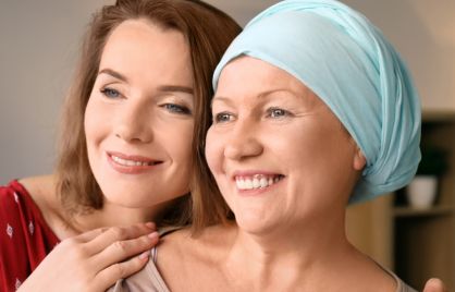 Two women, one of which is a cancer patient, are hugging and smiling.
