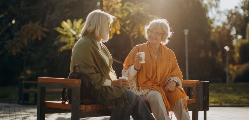 Two middle age women chatting on a park bench