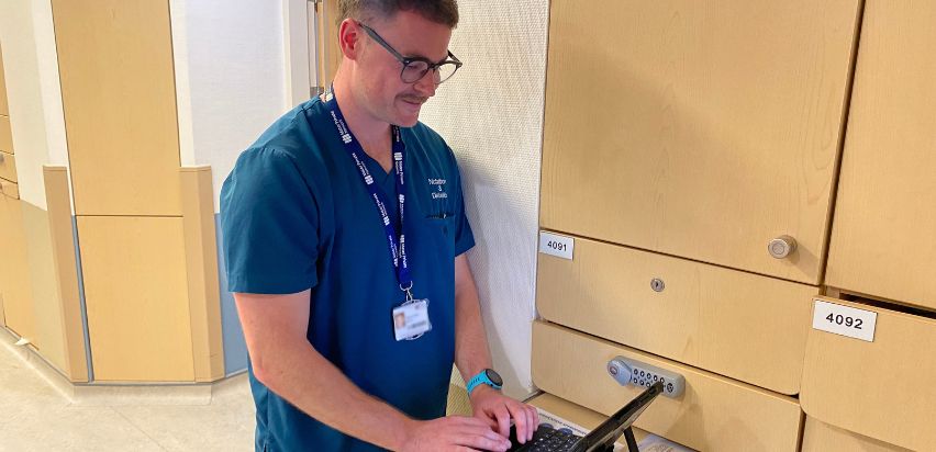 A man in a blue healthcare uniform looking at a tablet.