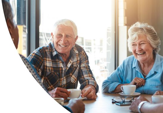 Older man and woman sitting at a table, chatting to another person