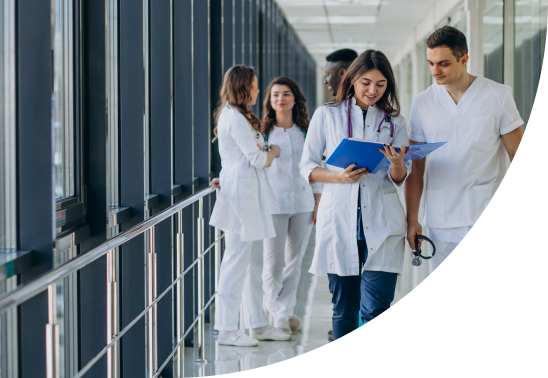 A female and male medical professionals walking down a hospital corridor, looking at a patient chart.